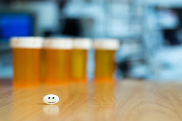 A pill with drawn happy face over a table and front empty bottle of medicine and copy space