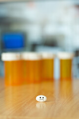 Vertical view of pill with drawn sad face over a table and front empty bottle of medicine and copy space