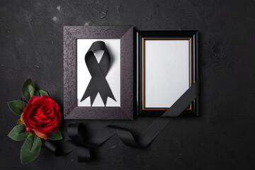 top view of picture frames with black bow and red flower on the dark surface funeral death