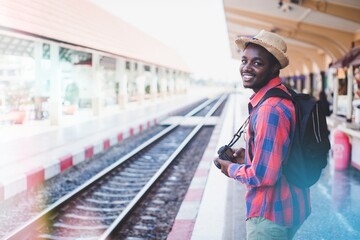 African backpackers wearing hats and cameras waiting for a train at a station to travel.Adventure travel concept