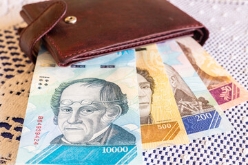 Venezuelan money sticking out of a brown wallet, lying on a table on a white tablecloth, Home budget and finance concept