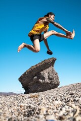 Man is mid-air while jumping over a weathered rock formation