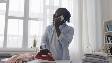 Distracted man talking on phone not paying attention to hot iron on clothes