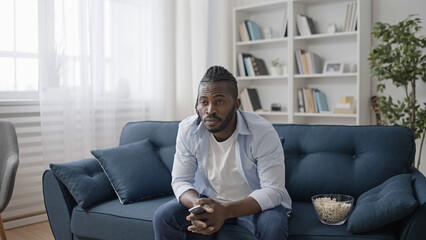 Relaxed man watching sitcom, sitting on sofa at home and eating popcorn