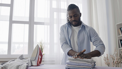 African American man carefully folding ironed clothes, enjoying neatness