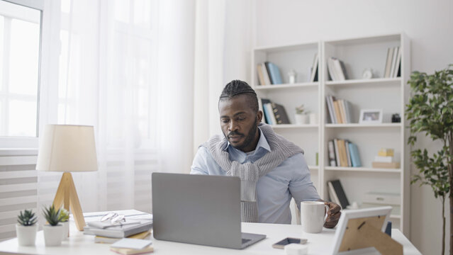 A concentrated African American man is a software developer working on his laptop in his office