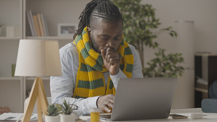 African American man in scarf coughing while working on laptop, flu, common cold