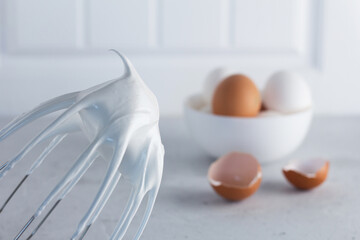 Whisked egg whites - whipped Italian meringue on a wire whisk and eggs on a gray background. copy...