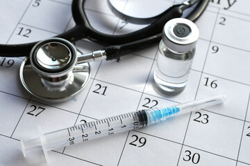 Schedule immunizations booster shot concept - syringe medicine vial stethoscope on calendar -...