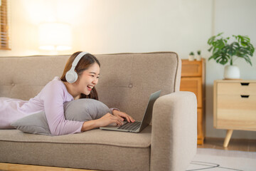 Obraz premium Happy young teenage beautiful Asian woman using tablet for home entertainment while sitting on the couch in the house.