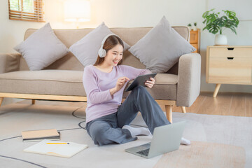 Happy young teenage beautiful Asian woman using tablet for home entertainment  while sitting on the couch in the house.