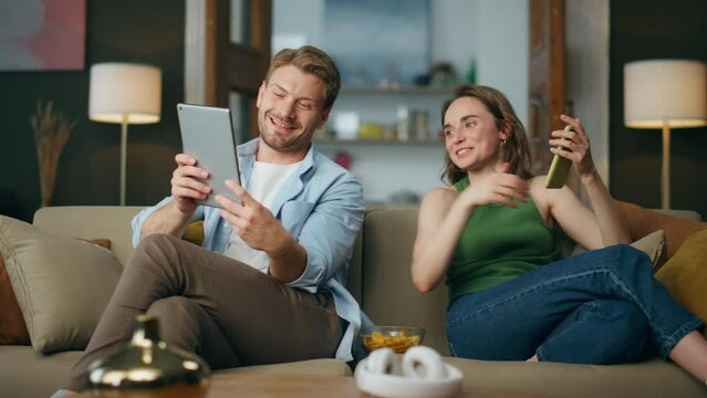 Happy woman talking husband pointing tablet indoors. Handsome man laughing joke