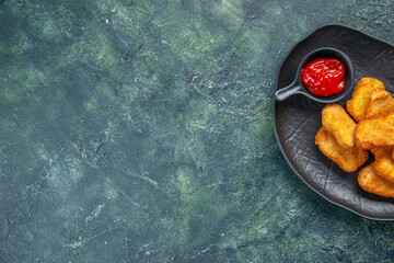 Half shot of tasty chicken nuggets and ketchup in black plate on the left side on dark background with free space