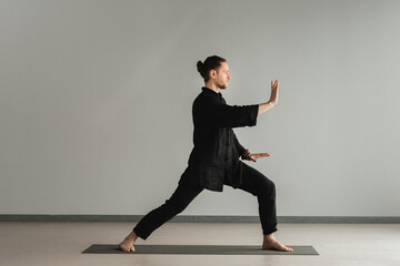 A man in black kimano practicing qigong energy exercises indoors - obrazy, fototapety, plakaty