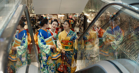 Three beautiful japanese geishas in traditional kimono dresses walking in shopping centre, standing...