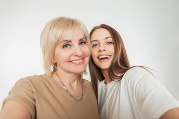 Beautiful happy young daughter woman with a smile and a cheerful elderly pretty mother take a selfie photo together on a white background in the studio