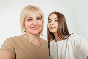 Beautiful family happy elderly mother with smile and daughter take a selfie photo on a smartphone on a white background in the studio
