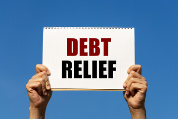 Debt relief text on notebook paper held by 2 hands with isolated blue sky background. This message can be used as business concept about debt relief.