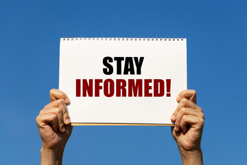 Stay informed text on notebook paper held by 2 hands with isolated blue sky background. This message can be used as business concept about staying informed.