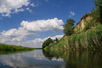 Fototapeta na wymiar A riverbed with steep banks and a summer blue sky with cumulus clouds.