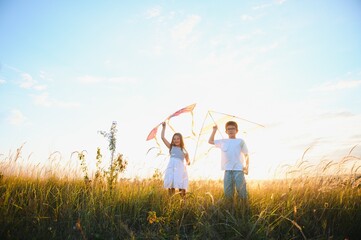 Happy children launch a kite in the field at sunset. Little boy and girl on summer vacation.