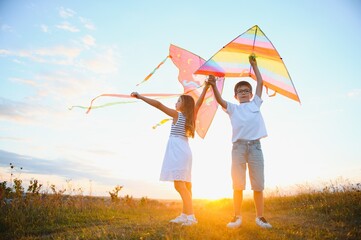 Happy children launch a kite in the field at sunset. Little boy and girl on summer vacation.
