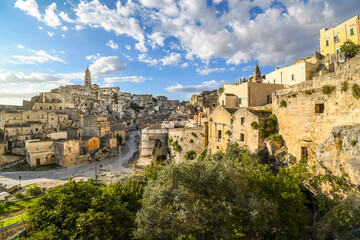 Fototapeta na wymiar Hillside view of the ancient city of Matera, Italy in the Basilicata region, including the old town, tourist street and mountain path, Sasso Barisano tower and the steep ravine canyon below.