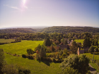 Obraz premium Drone photo of houses between trees and mountains in Belgium, beautiful horizon view
