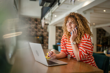 Woman use smartphone make a call talk while work on laptop from cafe