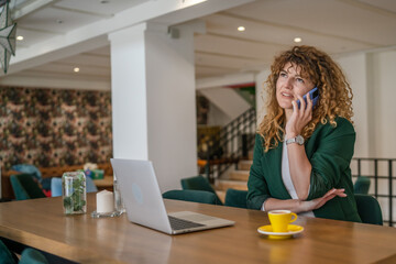 Woman use smartphone make a call talk while work on laptop from cafe