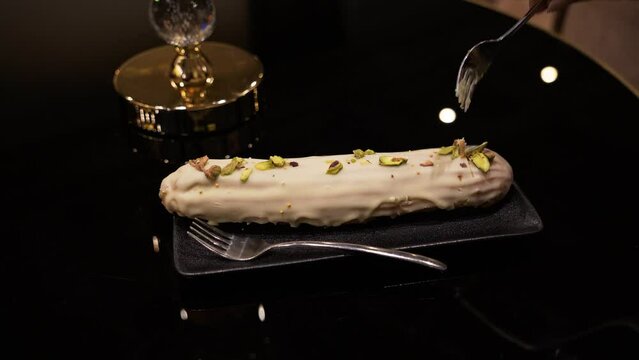 Person cutting a sweet eclair with green cream inside on the black table