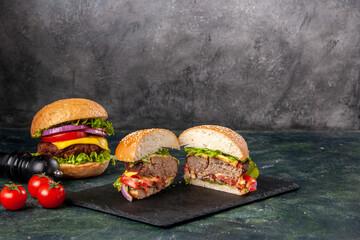 Top view of whole cut various tasty sandwiches and tomatoes on black tray on gray blurred background