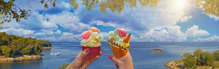 Wonderful romantic summer afternoon landscape panorama of a couple with beautiful bright sweet ice cream of different flavors in the hands and sea on background. Green lagoon sea bay in Porec, Croatia - 594758316