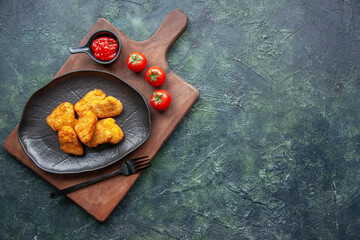 Top view of chicken nuggets on a black plate and fork on wooden board tomatoes ketchup on the right side on dark background with free space