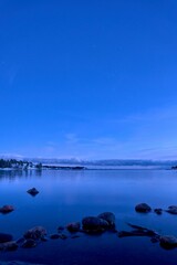 Vertical shot of vibrant blue toned sunset above tranquil sea waters seen through the rocky shore