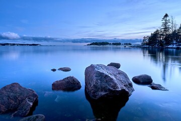Scenic vibrant blue toned sunset above tranquil sea waters seen through the rocky shore