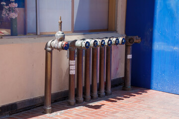 Many brass fire stand pipes are side by side and are coming from from a brick ground surface. There...