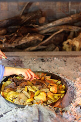 Unrecognizable person preparing meat and potatoes under the iron bell ('peka') in the fireplace. Traditional rural meal in Croatia. Selective focus.