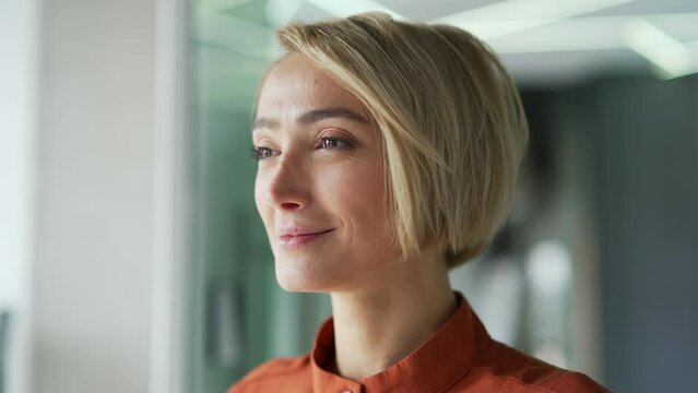 Close up portrait. Young blonde woman relaxing with closed eyes in a modern office. Beautiful businesswoman takes a deep breath, smiles, took a break from work. Female employee rests at the workplace