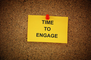 A yellow paper note with the words Time To Engage on it pinned to cork board