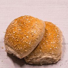 Two brown wheaten Oatmeal rolls on top[ of a wooden board