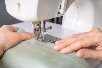 Female hands stitching white fabric on modern sewing machine at workplace in atelier