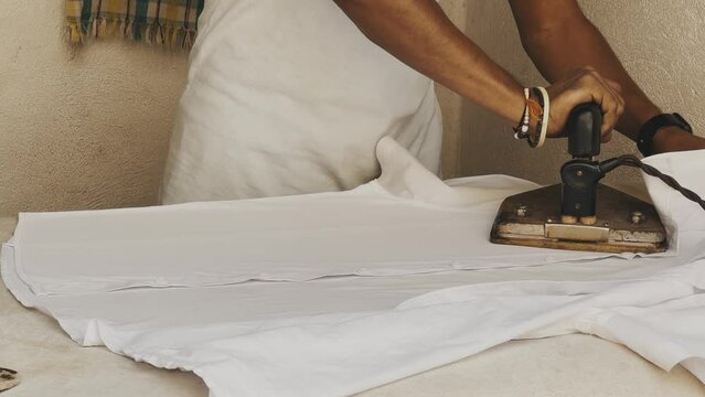 A man ironing a white t-shirt with an old iron, India