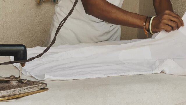 A man ironing a white t-shirt with an old iron, India
