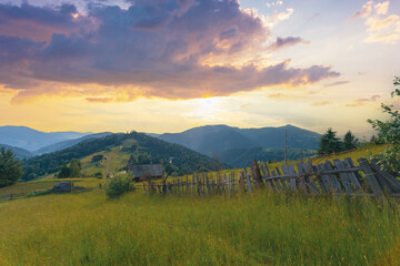 Idyllic rural scenery in the Carpathian mountains, Ukraine. An old wooden fence goes along the pathway on the high grass hill under the bright sunset sky.