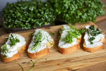 Closed image of a canapes with sour cream and mixed fresh microgreens on a wooden plate arranged on a wooden table.