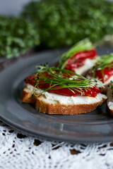 Closeup of sandwiches for breakfast with slice of whole grain bread, cream cheese, mixed microgreens  and roasted red pepper garnished on grey plate.