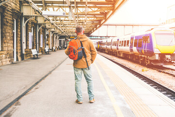 Fototapeta premium Traveler with a backpack waiting for a train at the train station. Travel concept.