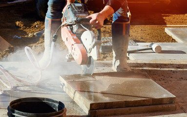 Builder cutting concrete slabs with petrol concrete saw and a diamond blade during external footpath paving works close up