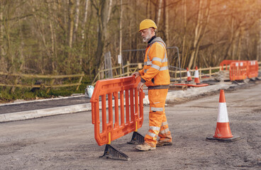 Builder placing safety barriers and red traffic cones during roadworks